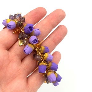 May include: A purple and yellow flower charm bracelet with gold accents. The bracelet is made of polymer clay and features a cluster of small flowers.