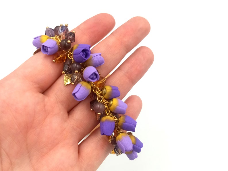 May include: A purple and yellow flower charm bracelet with gold accents. The bracelet is made of polymer clay and features a cluster of small flowers.