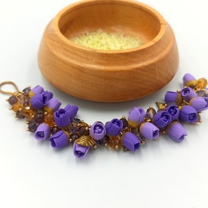 May include: A purple flower bracelet with gold accents and clear beads. The bracelet is made of polymer clay and is a beautiful and unique piece of jewelry.