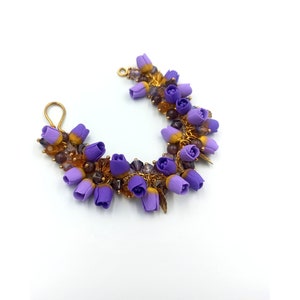 May include: A purple and gold flower bracelet with small purple flowers and gold beads. The bracelet is made of wire and has a hook closure.