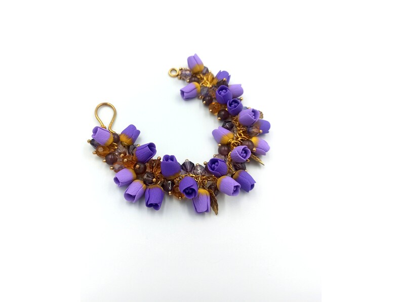 May include: A purple and gold flower bracelet with small purple flowers and gold beads. The bracelet is made of wire and has a hook closure.