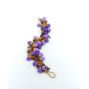 May include: A purple and gold beaded bracelet with a floral design. The bracelet is made with small purple and gold beads, and the flowers are made of purple and gold fabric.
