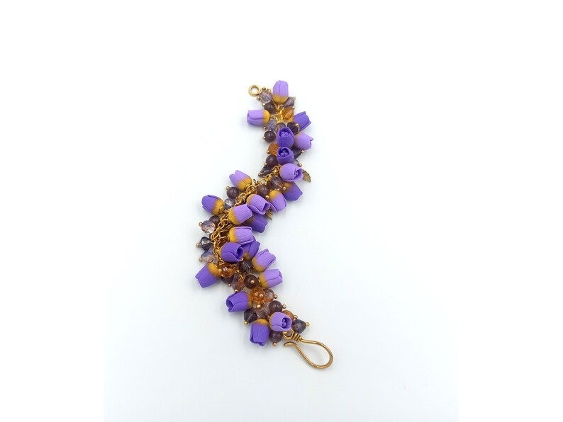 May include: A purple and gold beaded bracelet with a floral design. The bracelet is made with small purple and gold beads, and the flowers are made of purple and gold fabric.