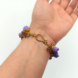 May include: A purple and gold beaded bracelet with a flower charm. The bracelet is made with small glass beads and has a gold clasp.