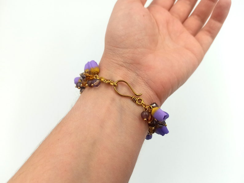 May include: A purple and gold beaded bracelet with a flower charm. The bracelet is made with small glass beads and has a gold clasp.