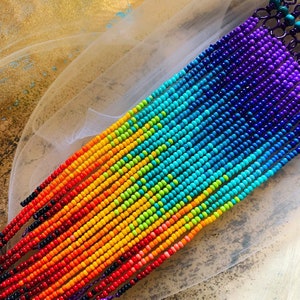 Peut inclure: Gros plan sur des bijoux de perles colorées disposés en arc-en-ciel. Les perles passent du rouge à l'orange, au jaune, au vert, au bleu et au violet. Les perles sont enfilées, créant un design vibrant et accrocheur.