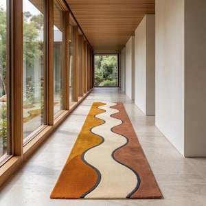 Könnte beinhalten: Ein langer, rechteckiger Läufer mit einem wellenförmigen, mehrfarbigen Muster in Senfgelb, Creme und Terrakottabraun. Das Design besteht aus fließenden, geschwungenen Linien, die durch dünne dunkelgraue Ränder getrennt sind und einen rhythmischen, organischen Fluss auf der Textiloberfläche erzeugen.