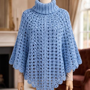 May include: A light blue crochet poncho featuring a high turtleneck collar and an intricate openwork diamond pattern. The garment has a vertical ribbed seam down the center front and a scalloped edge along the hemline, displayed on a mannequin.