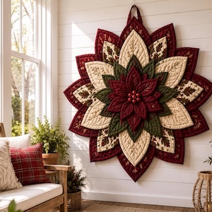 May include: A large, circular, quilted wall hanging shaped like a poinsettia flower. It features layered, pointed petals in deep burgundy, cream, and forest green, with a central cluster of small, round, red berries. The fabric has quilted textures.