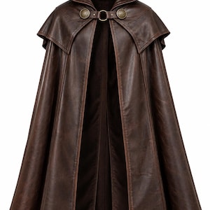 May include: A dark brown hooded cloak featuring a smooth, weathered texture. The garment includes a short shoulder capelet, a central ring closure, and two circular metallic fasteners with intricate embossed patterns on the front collar area.