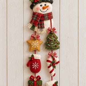 May include: A felt wall hanging featuring a snowman wearing a black hat and plaid scarf, with two vertical strings of ornaments including a yellow star, green tree, red mitten, candy cane, green gift box, and a red stocking with white trim.