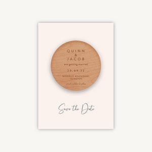 May include: A wooden save the date card with a round wooden disc featuring the names Quinn & Jacob, the date 20.09.22, and the location Waverley Boathouse, Islington. The text "Save the Date" is written in cursive below the disc.