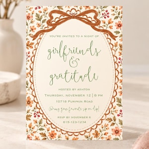 May include: A rectangular invitation card featuring a cream background with a floral border of orange flowers and red berries. A brown ribbon bow sits at the top. The text reads: You're invited to a night of girlfriends & gratitude hosted by Ashton.
