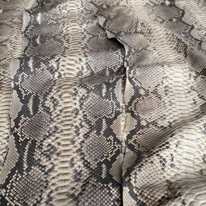 Könnte beinhalten: Ein großes, flaches Stück natürliche Pythonhaut mit einem detaillierten, sich wiederholenden rautenförmigen Schuppenmuster in Beige-, Grau- und Dunkelbrauntönen. Die Oberfläche weist eine strukturierte, organische Oberfläche mit dem Text BestExoticTannery auf.