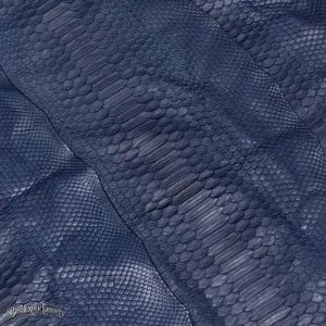 May include: A dark navy blue snakeskin leather hide featuring a distinct central row of large, elongated scales flanked by smaller, tightly packed diamond-shaped scales. The surface displays a natural texture with the text BestExoticTannery visible.