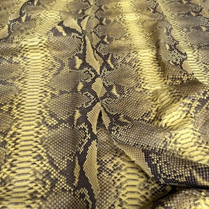 May include: A large, flexible sheet of genuine snakeskin leather featuring a natural, repeating scale pattern in shades of mustard yellow, olive green, and dark brown. The surface displays a textured, organic finish with the text BestExoticTannery.