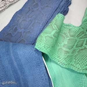 Puede incluir: Varias láminas de piel de serpiente texturizada en tonos azules y verdes. El cuero azul presenta un patrón de escamas oscuro y repetitivo, mientras que el cuero verde muestra una textura de escamas vibrante y más clara. El texto BestExoticTannery es visible.