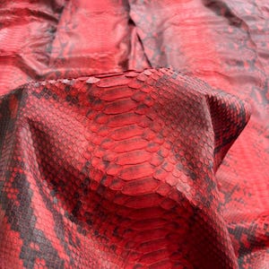 Puede incluir: Una pieza grande de cuero de piel de serpiente roja y negra con un patrón de escamas distintivo. La superficie muestra una base roja vibrante con marcas negras oscuras. El texto BestExoticTannery está impreso en la esquina inferior izquierda.