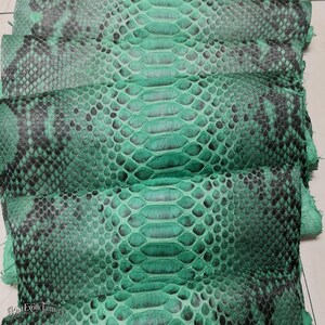 Puede incluir: Una pila de láminas de piel de serpiente en color verde esmeralda y negro con un patrón de escamas reptilianas. La superficie muestra un degradado de tonos verdes vibrantes que transicionan a marcas gris oscuro. El texto Best Exotic Tannery es visible.