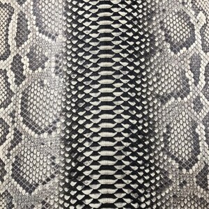 May include: A textured surface featuring a repeating snakeskin pattern in shades of black, white, and gray. The design displays a central vertical column of larger, elongated scales flanked by smaller, rounded scales on both sides.
