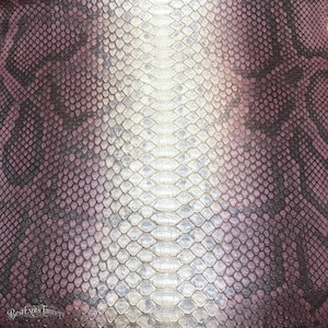 May include: A sheet of snakeskin leather featuring a gradient pattern that transitions from a dark purple and black outer edge to a light, off-white centre. The texture consists of small, overlapping scales with the text Best Exotic Tannery.