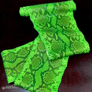 Puede incluir: Una piel de serpiente de cuero en color verde neón vibrante que presenta un patrón distintivo y repetitivo de escamas en forma de diamante. El material muestra una superficie texturizada con tonos variados de verde lima brillante y verde oscuro.