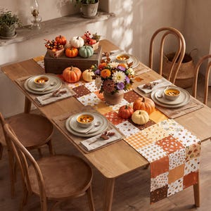 Può includere: Un tavolo da pranzo in legno apparecchiato per quattro persone con un runner patchwork dai motivi autunnali arancioni, bianchi e marroni. Il tavolo include coperti con ciotole di zuppa, un centrotavola floreale e zucche decorative.