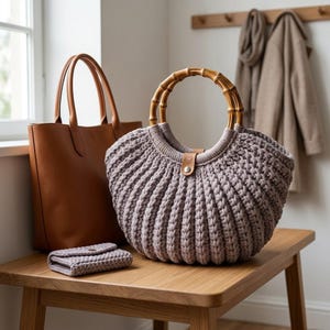 May include: A mauve crocheted handbag with a rounded bamboo handle and a small leather tab closure, positioned next to a smooth brown leather tote bag and a small matching mauve crocheted wallet, all featuring a textured, ribbed knit pattern.
