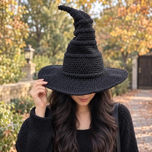 May include: A black crocheted witch hat with a tall, pointed, slightly curved crown and a wide, circular brim. The hat features a textured, hand-stitched yarn construction with a consistent dark black colour throughout the entire piece.