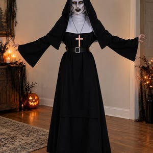 Pode incluir: Um traje de freira em preto e branco de corpo inteiro, com um hábito longo preto de mangas largas, uma touca branca, um véu preto e um cinto preto com fivela prateada. Um crucifixo de madeira pende de um cordão preto ao redor do pescoço.