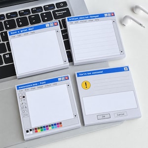 May include: Four square sticky note pads featuring retro computer interface designs. The designs include a blank notepad, a lined notepad labeled brilliant_ideas.txt, a paint program interface labeled masterpiece.bmp, and a dialog box saying You're too awesome!