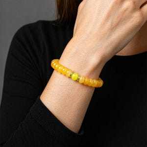 May include: A stretch bracelet composed of numerous small, translucent amber-colored beads. The bracelet features a single, bright lime-green spherical bead at the center, flanked by two small, polished silver-toned metal spacer rings.