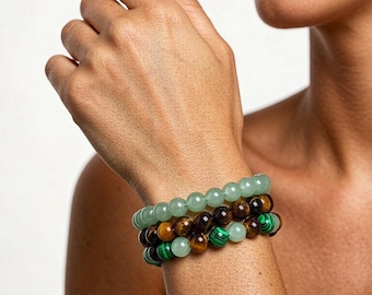 Peut inclure: Un empilement de trois bracelets de perles composées de pierres rondes et lisses. Un rang est constitué de perles d'aventurine vert clair, tandis que les deux autres mélangent des perles d'œil de tigre brun et de malachite verte.