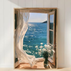 以下が含まれることがあります： 輝く青い海と遠くの岩の島を見渡す開いた窓を描いた額入りウォールアートプリント。透き通った白いカーテンが内側に揺れ、白い花を生けたガラスの花瓶が手前の窓枠に置かれています。