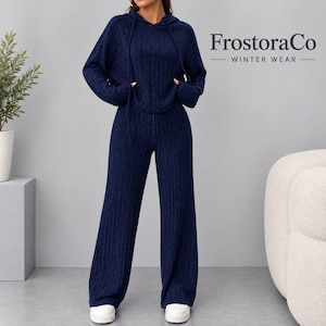 May include: A dark blue ribbed knit two-piece set consisting of a long-sleeve hooded sweatshirt with drawstrings and matching wide-leg trousers. The text "FrostoraCo WINTER WEAR" is printed in black on the upper right side of the image.