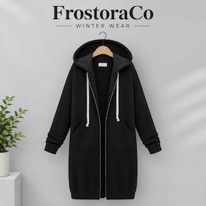 May include: A long-length black zip-up hoodie featuring a hood with white drawstrings, long sleeves with ribbed cuffs, and two front pockets. The garment is displayed on a hanger with the text FrostoraCo WINTER WEAR visible above it.