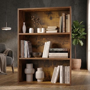 May include: A three-tier wooden bookshelf with a dark brown wood grain finish. The shelves are filled with various books, including one titled Chemistry, and several white decorative vases and containers. The unit has an open back design.