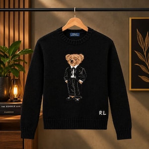 Könnte beinhalten: Ein schwarzer Langarmpullover mit Rundhalsausschnitt und einem gestrickten Motiv eines Teddybären im Smoking mit Fliege. Der Pullover hat einen gerippten Kragen, Bündchen und Saum sowie die weiß gestickten Buchstaben RL auf der rechten Seite.