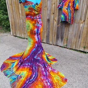 Puede incluir: Un vestido tie-dye con falda de sirena y una camiseta tie-dye a juego. El vestido es una mezcla vibrante de naranja, amarillo, morado y azul.