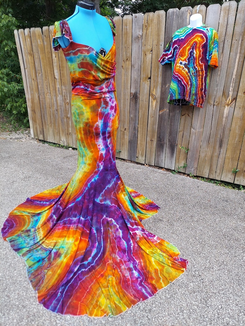 Puede incluir: Un vestido tie-dye con falda de sirena y una camiseta tie-dye a juego. El vestido es una mezcla vibrante de naranja, amarillo, morado y azul.