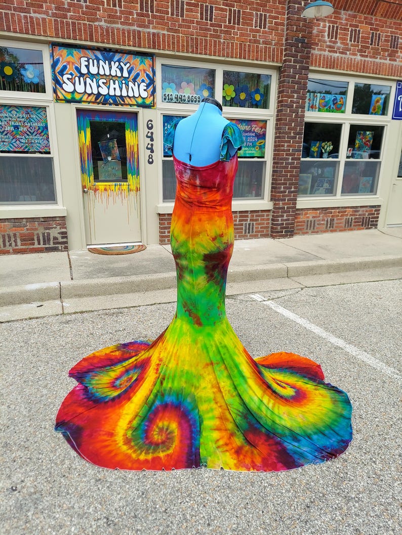 Puede incluir: Un vestido largo y fluido de tie-dye con una falda de estilo sirena. El vestido es una mezcla de colores brillantes, incluyendo rojo, naranja, amarillo, verde, azul y morado. El vestido est&aacute; hecho de una tela suave y el&aacute;stica y tiene un ajuste c&oacute;modo.