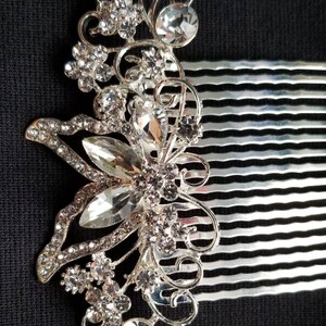 May include: Silver hair comb with a decorative design of a butterfly with clear rhinestones. The comb has a silver finish and is adorned with sparkling crystals.