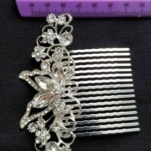 May include: Silver hair comb with a decorative butterfly design featuring clear rhinestones. The comb is approximately 2.5 inches long. The text "The Bling Co." is visible below the comb.