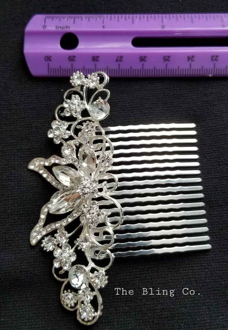 May include: Silver hair comb with a decorative butterfly design featuring clear rhinestones. The comb is approximately 2.5 inches long. The text "The Bling Co." is visible below the comb.