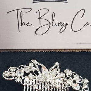 May include: Silver hair comb with a floral design and clear rhinestones. The comb has a row of teeth on the bottom.