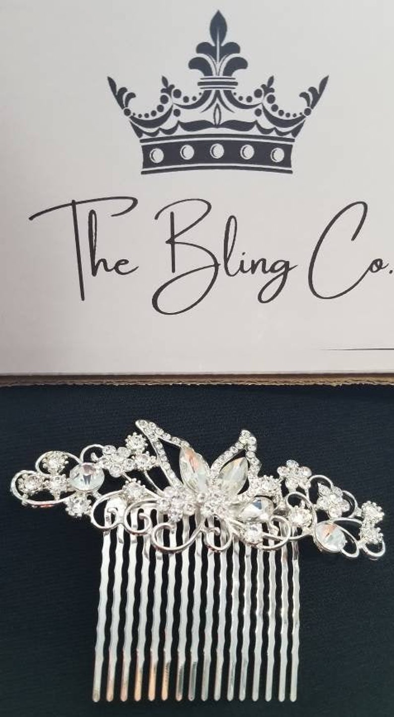 May include: Silver hair comb with a floral design and clear rhinestones. The comb has a row of teeth on the bottom.