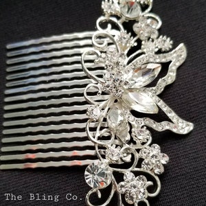 May include: Silver hair comb with a large rhinestone butterfly design. The comb has a row of teeth on the bottom and is decorated with clear rhinestones.