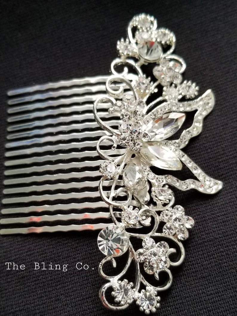 May include: Silver hair comb with a large rhinestone butterfly design. The comb has a row of teeth on the bottom and is decorated with clear rhinestones.
