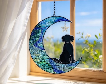 May include: A stained glass suncatcher shaped like a crescent moon with blue and green textured glass. A solid black silhouette of a dog sits on the moon, and a small silver-colored star hangs from the top curve by a metal chain.