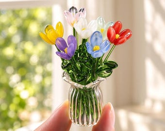 May include: A miniature glass flower arrangement featuring a bouquet of small, colorful blossoms in shades of red, yellow, blue, purple, white, and pink, with green glass stems and leaves, housed in a clear, vertically ribbed glass vase.